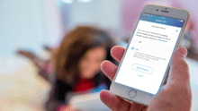 Parent holding smartphone with Xfinity xFi app open, showing parental control feature interface; child in the background.