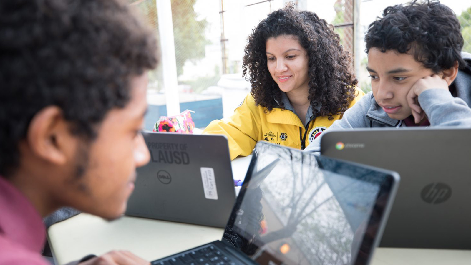 A female and two males sitting at a table working at their computers.