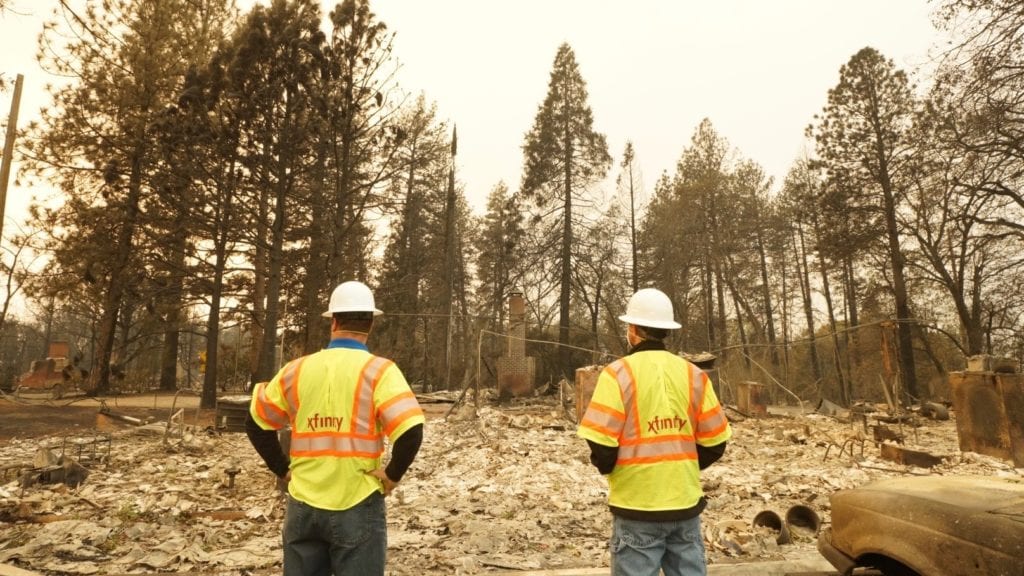 Two Xfinity technicians examine fire damage in a neighborhood