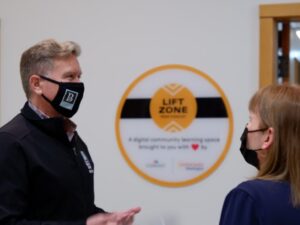 Bremerton Mayor Greg Wheeler, wearing a black mask, talks with Easterseals Washington President & CEO Cathy Bisaillon in front of a Comcast Lift Zone sign. 