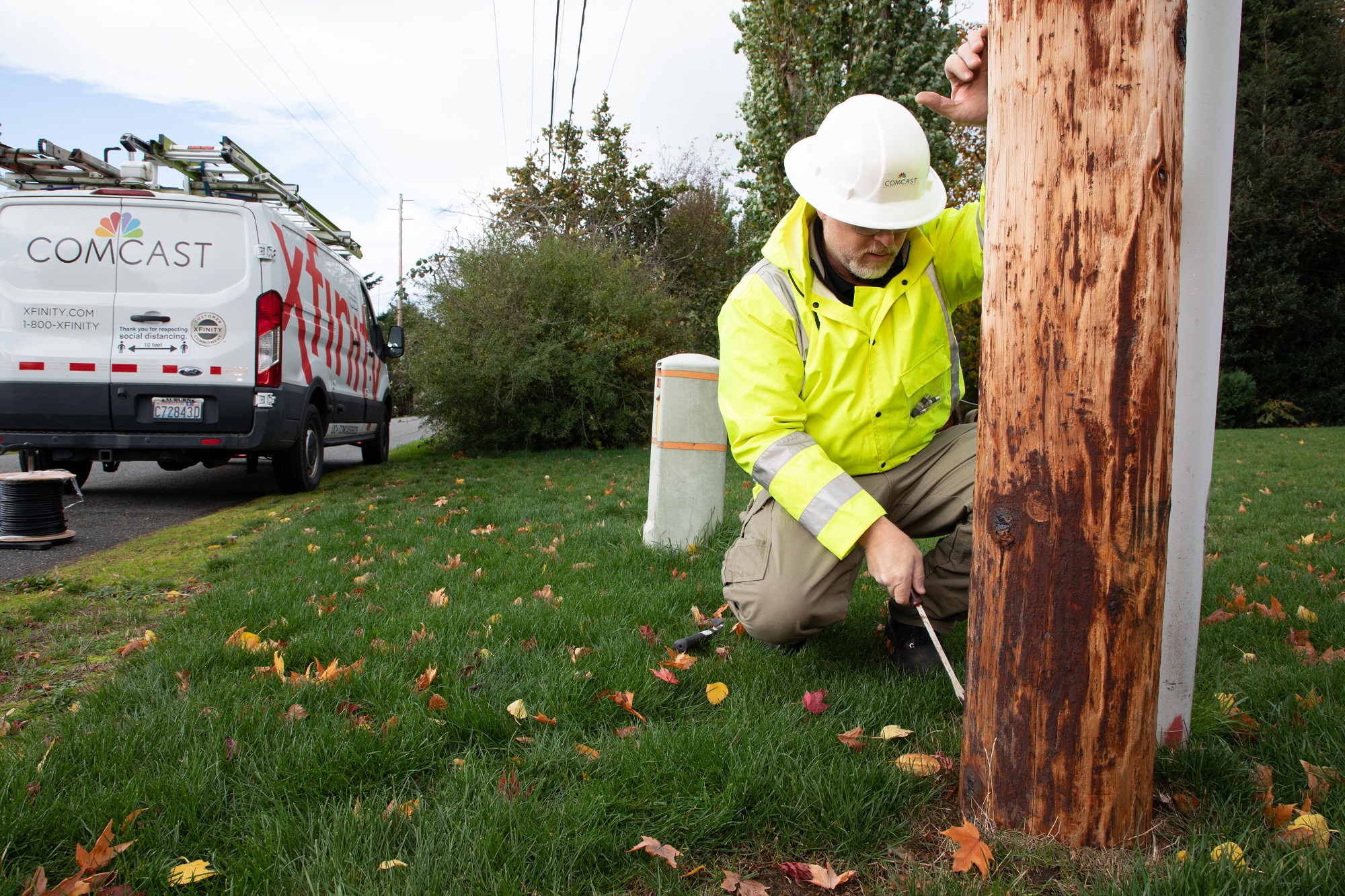 A Comcast technician works on a power pole next to a Comcast van.