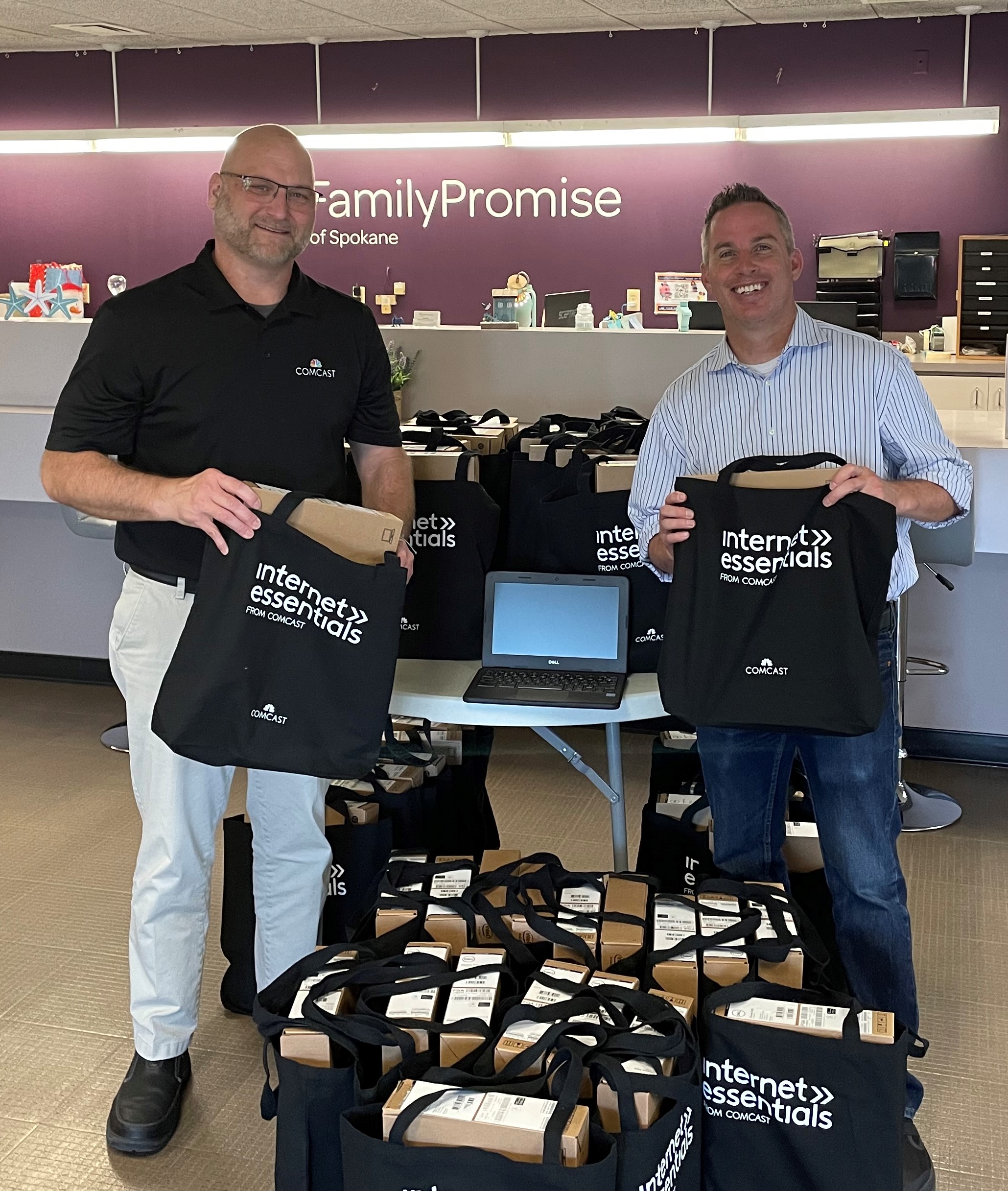 Representatives from Comcast and Family Promise of Spokane smile with bags with laptops in them at a Family Promise office.