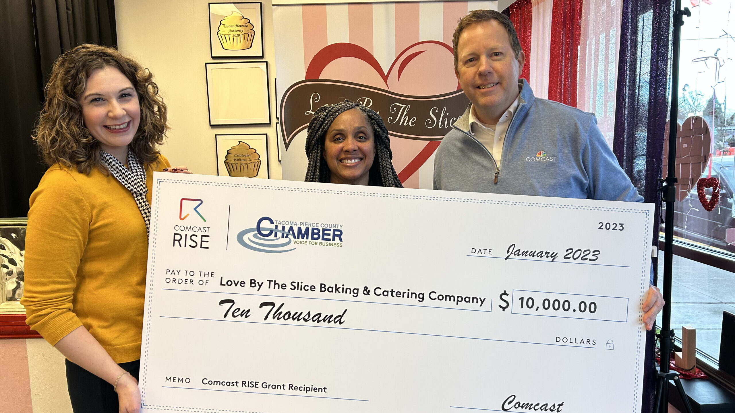 A woman holds a large check with a man and a woman in a store.