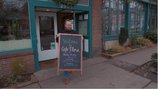 Nat Stratton-Clarke puts a chalk sign out in front of Cafe Flora on the sidewalk.