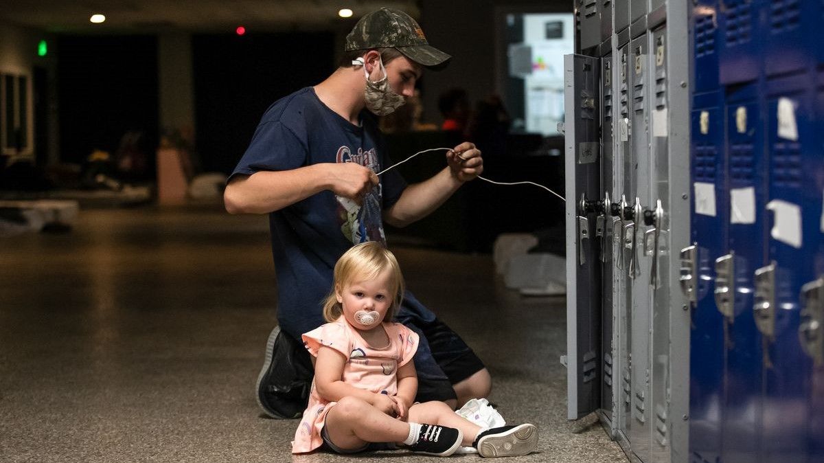 A young man and a young child sit by lockers in a shelter.