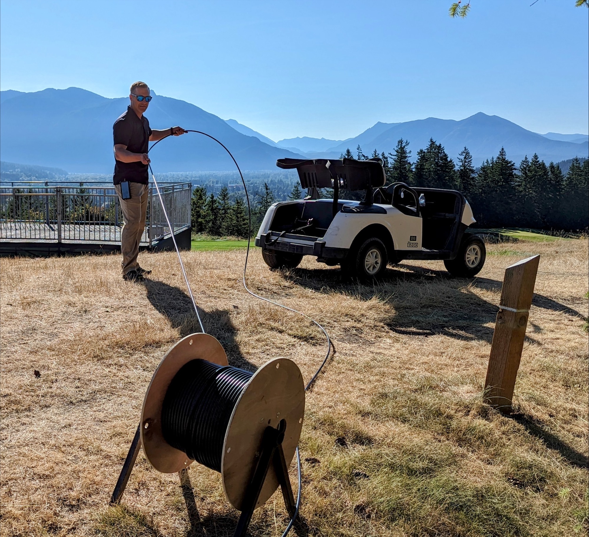 A Comcast technician works with cable on a golf course with a golf cart.