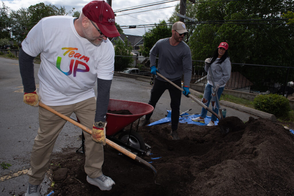 Three people shovel dirt in a parking lot. 