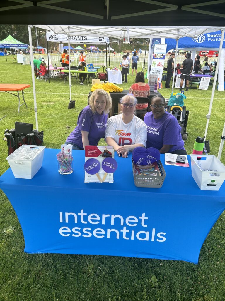 Three Comcast volunteers sit at an Internet Essentials table. 