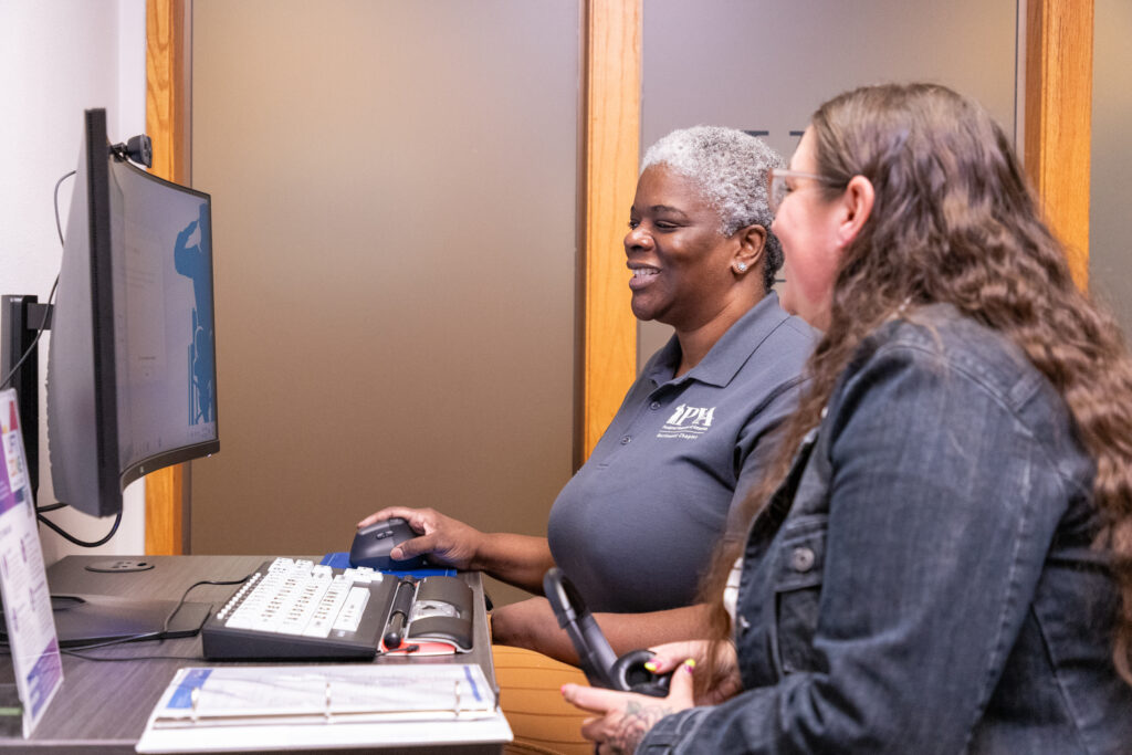 Two women smile and work at a computer.