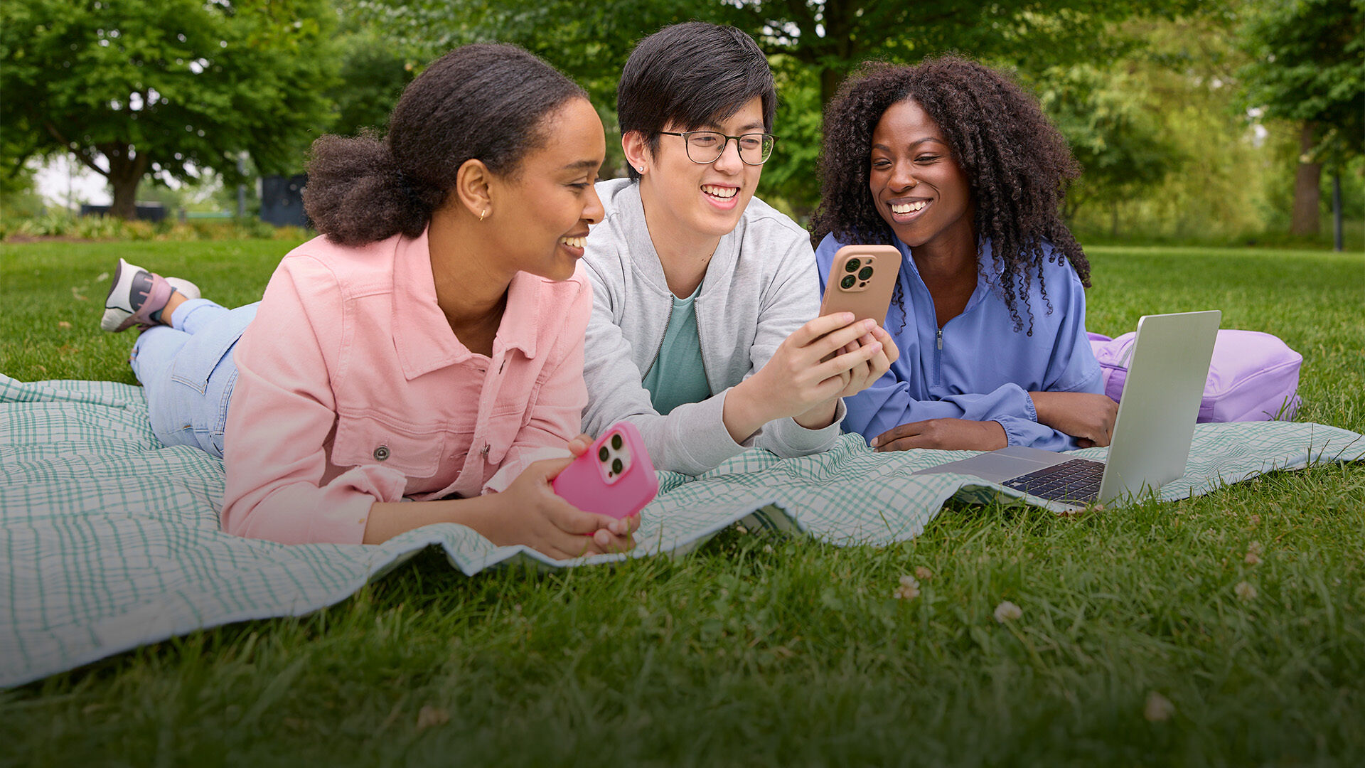 Three people in a park watching a phone.