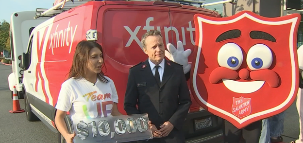Salvation Army and Comcast representatives with an Xfinity truck, the Salvation Army mascot, and a $10,000 sign.
